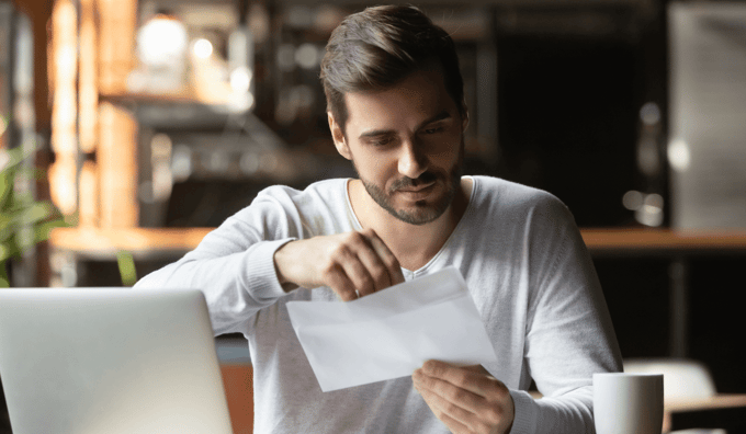 Man opening letter in envelope at desk with laptop and coffee