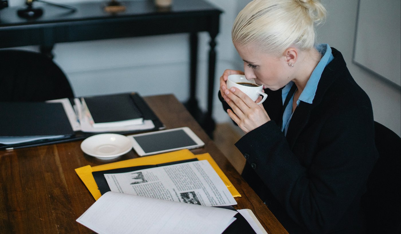 Woman in business attire sips coffee whilst reading legal documentation