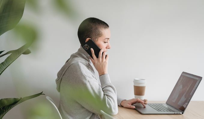 Woman with short hair takes a call whilst working from home as she works from her laptop