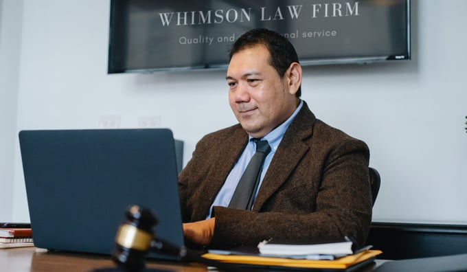 Man wearing a shirt and tie in the legal profession sits at his laptop under law firm sign