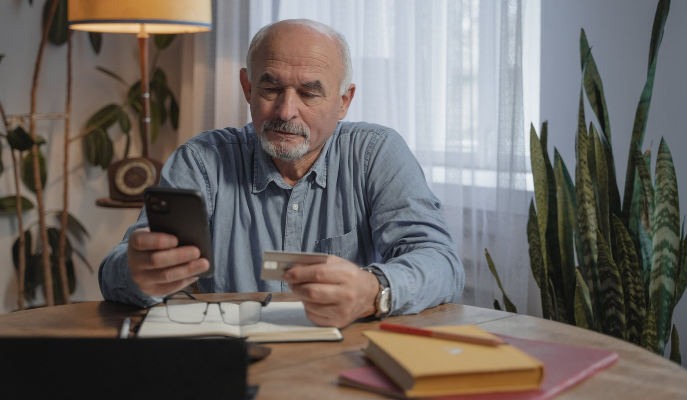 Older man wearing a blue shirt has his phone and credit card in hand